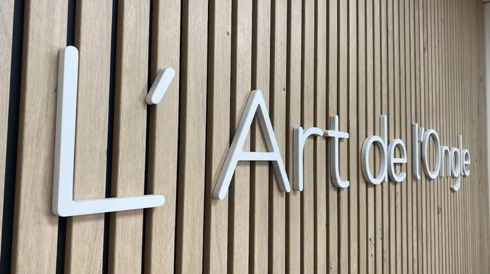 Enseigne L'Art de l'Ongle en lettres blanches sur un mur en lattes de bois